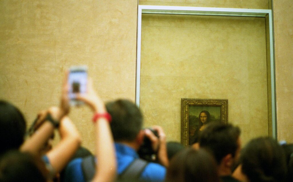 A crowd of people taking photos of the Mona Lisa, displayed behind protective glass in a museum.