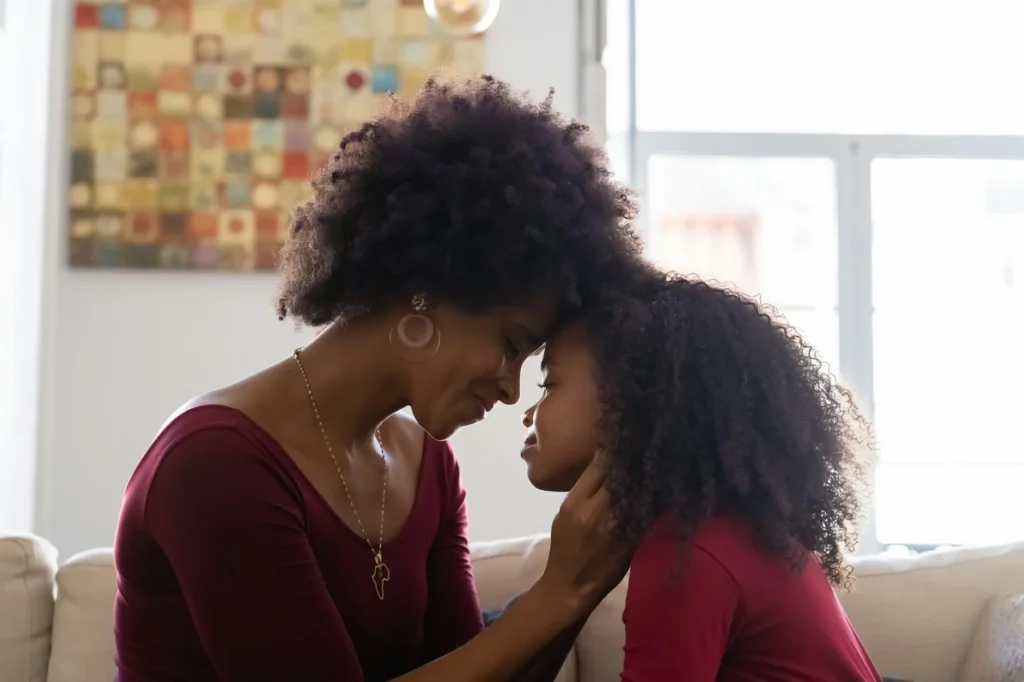 A mother and daughter sit closely together, touching foreheads in a moment of emotional connection and warmth.