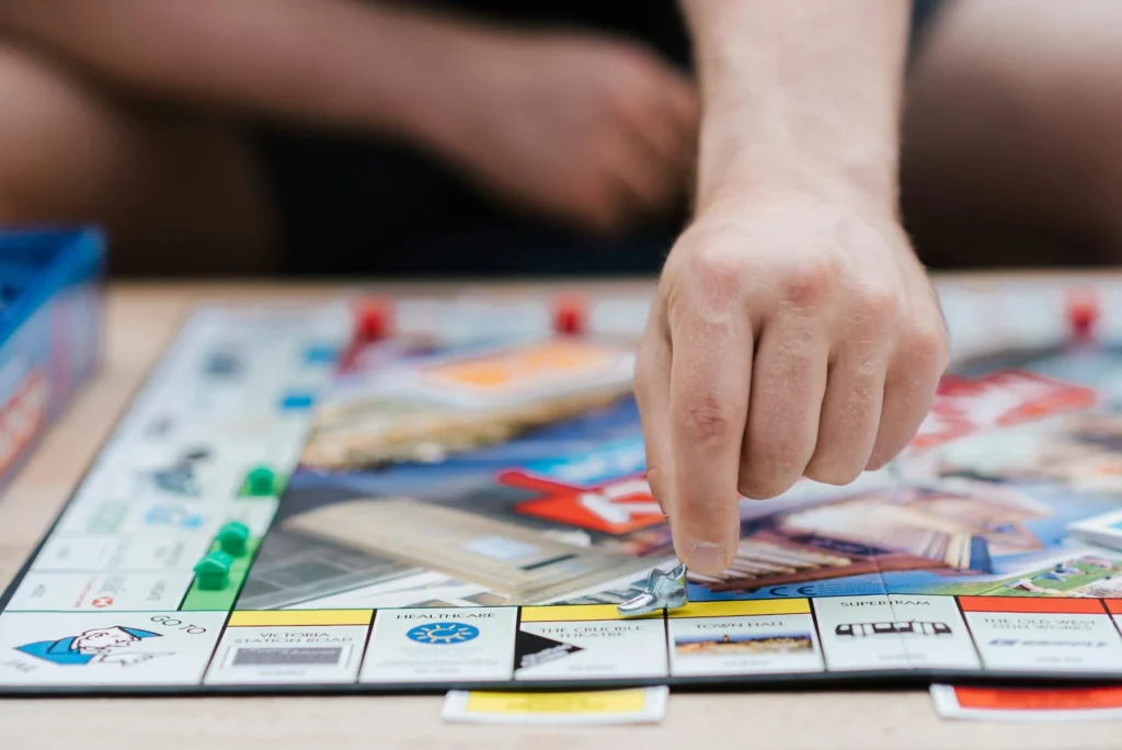 A person plays Monopoly, the famous board game, moving a piece across the board indoors.