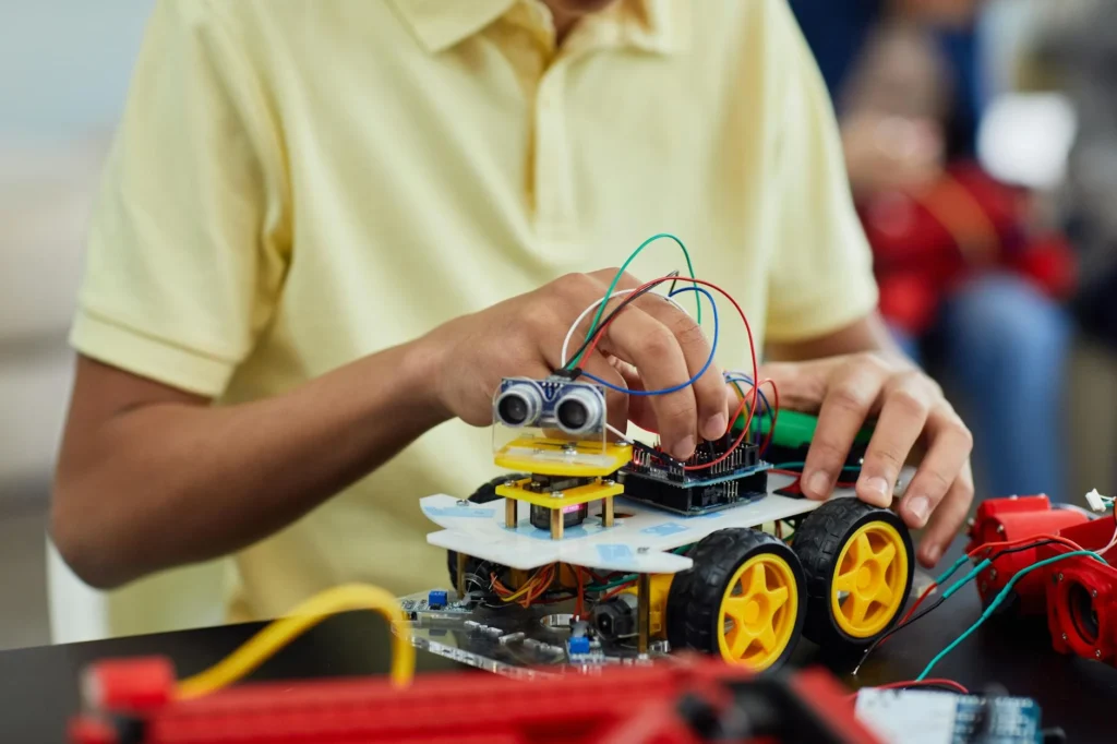 Close-up of a child assembling a wheeled robot with wires and sensors.