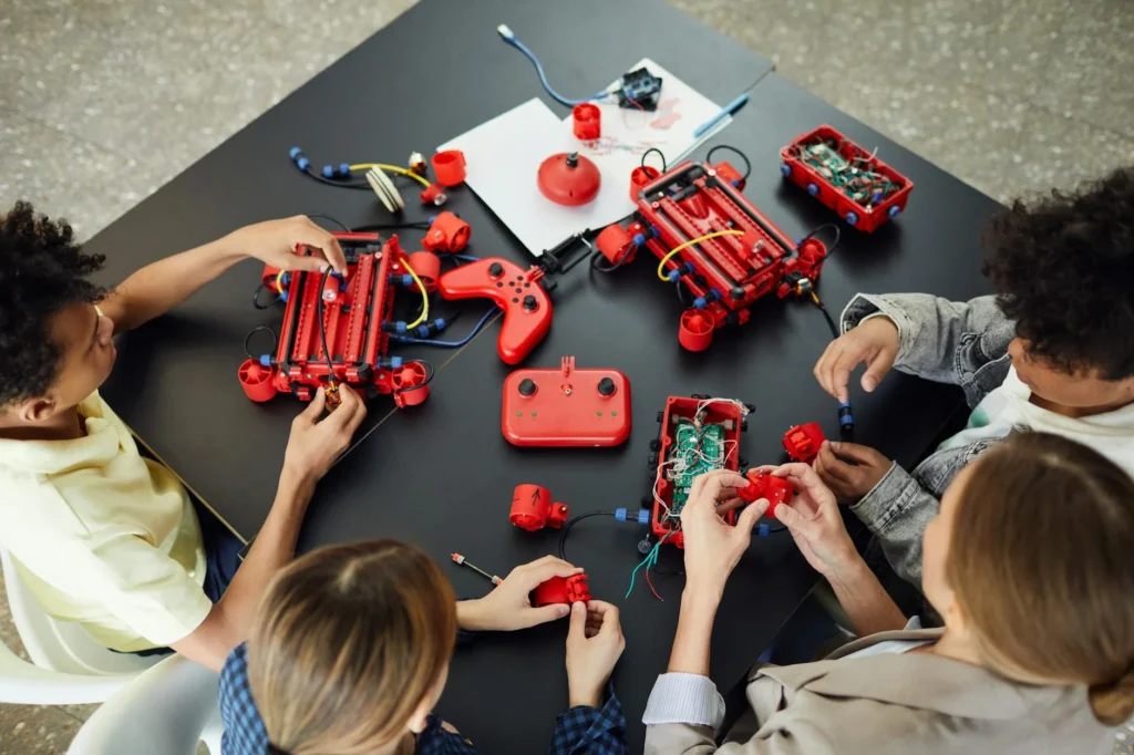 Group of children collaborating on building red robotic kits at a table.