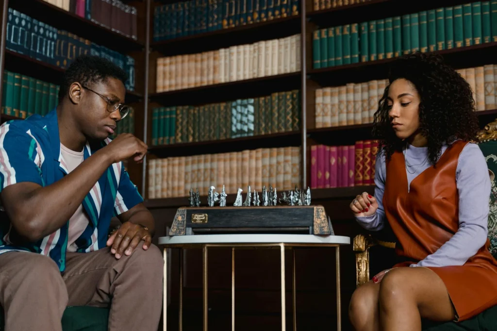 Two adults playing chess in a cozy library setting, focused and strategic atmosphere.