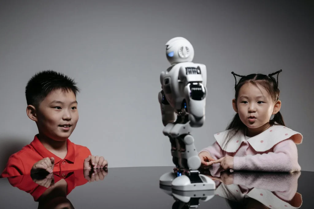 Two children excitedly interacting with a small humanoid robot on a reflective surface.
